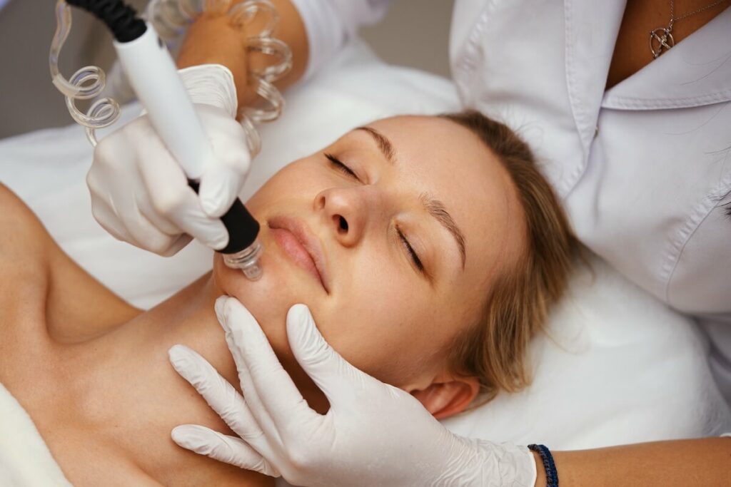 clinician shown administering Hydrafacial treatment with suction handpiece to deep cleanse skin.
